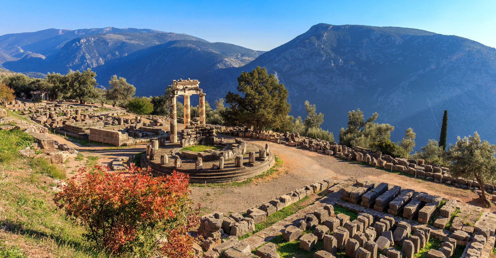 Ruins of the ancient Tholos temple at Delphi with mountains and clear blue sky