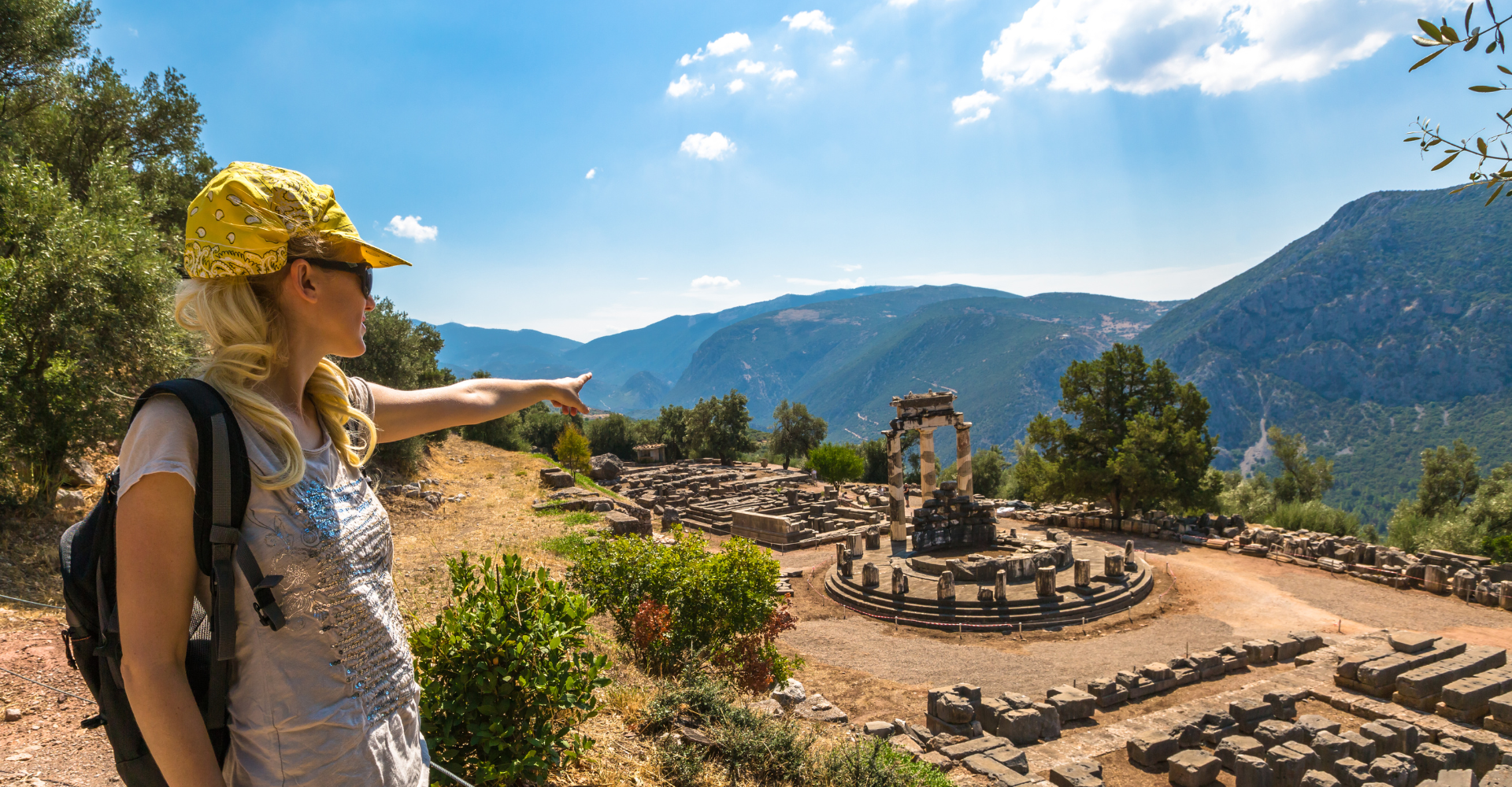 Tourist woman pointing at ancient Tholos temple ruins with mountains in Delphi
