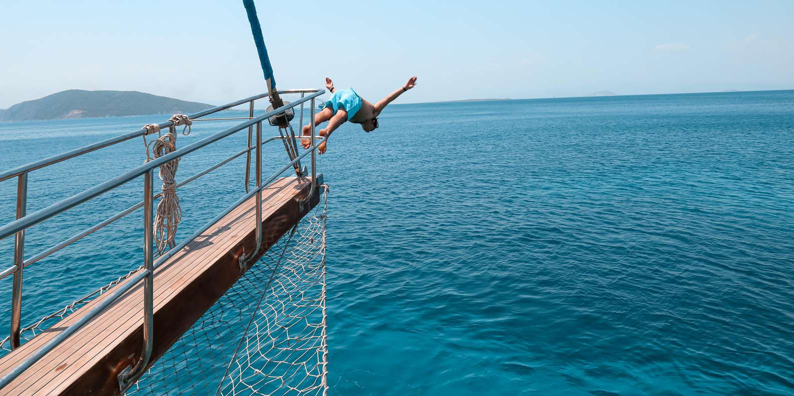 A kid diving into the clear blue Aegean waters from a cruiseship