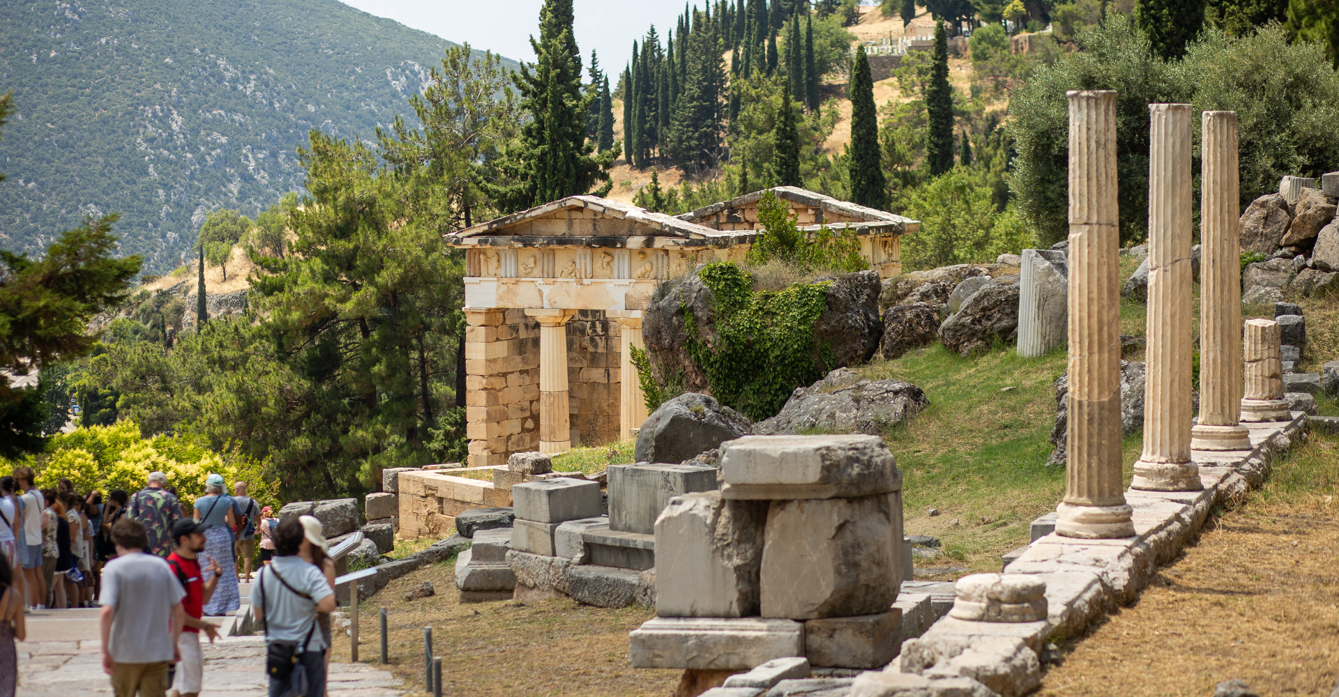 Ancient Greek ruins with stone columns and tourists in Delphi mountain landscape