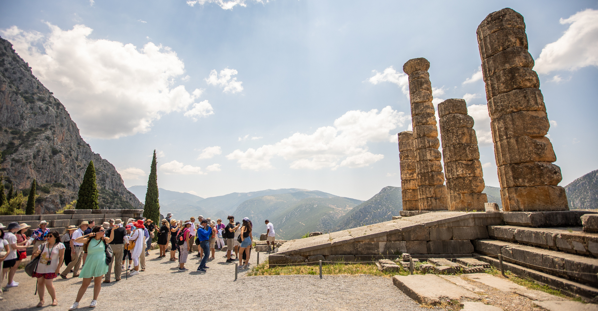 Tourists visiting ancient stone columns ruins at Delphi archaeological site with mountains