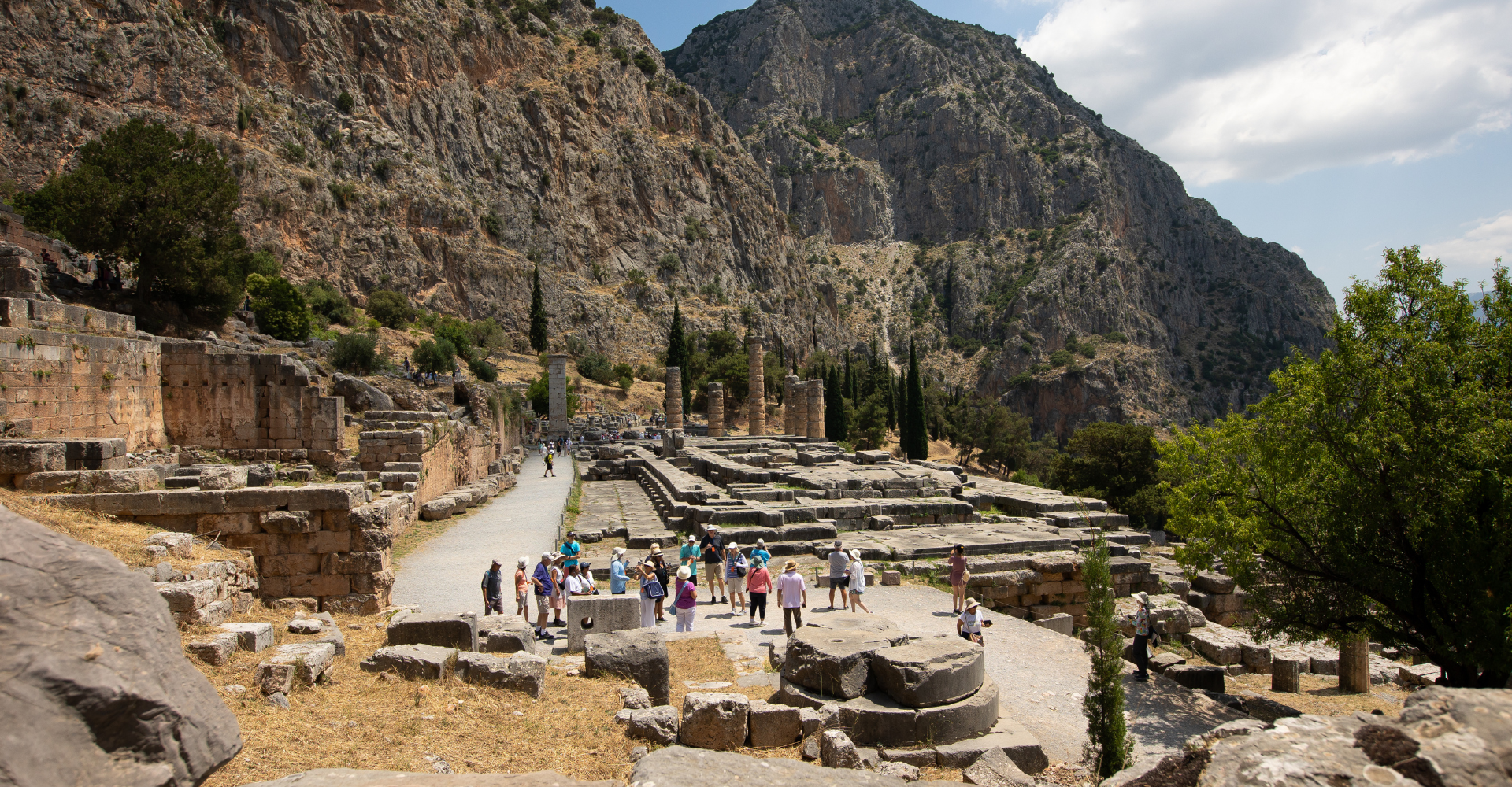 Tourists exploring the archaeological site of Delphi with ruins and mountainous landscape in central Greece