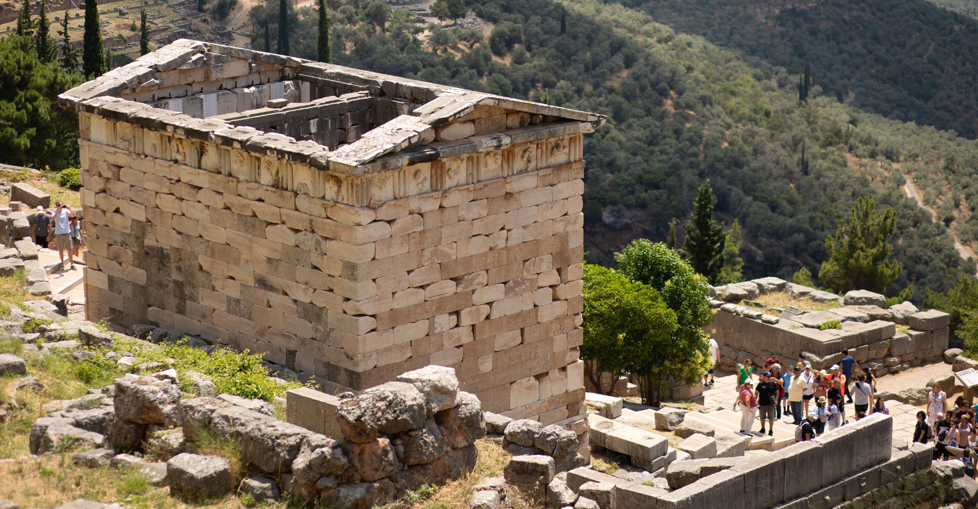 Ancient stone treasury building ruins with tourists at Delphi archaeological site